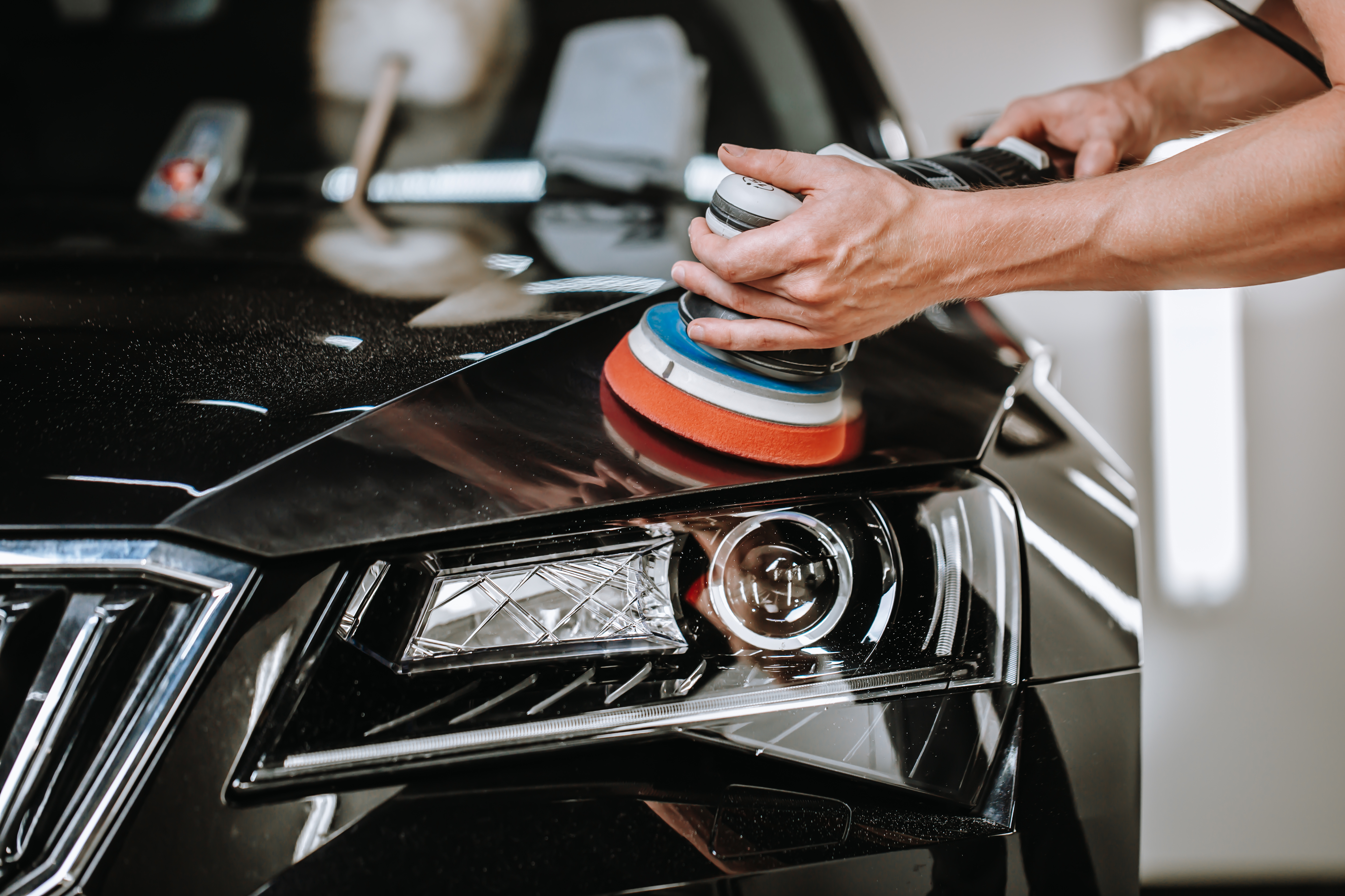 Person using polishing pad on black car hood during detailing service