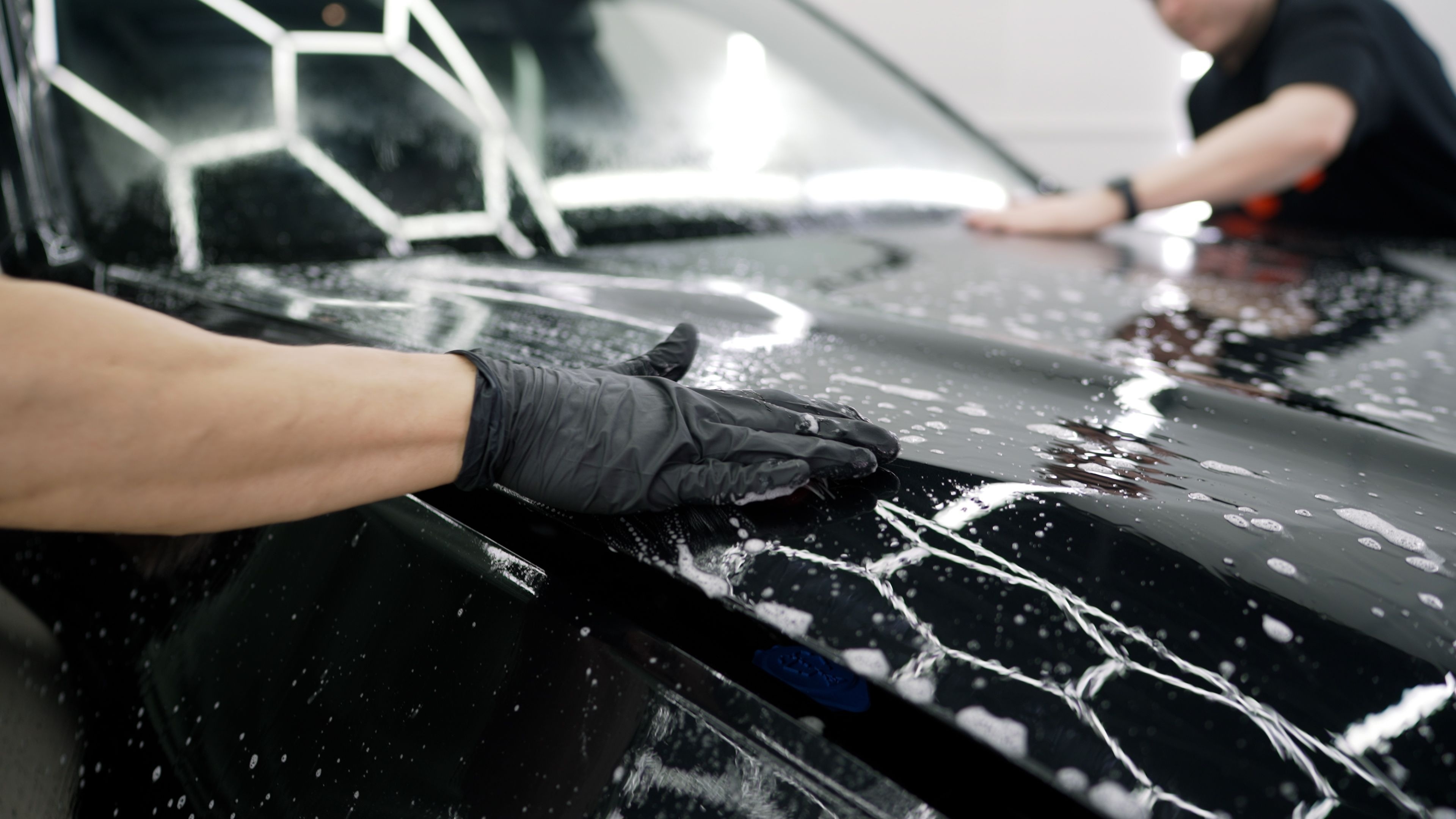 Workers wearing black gloves washing a black car with soapy water and foam