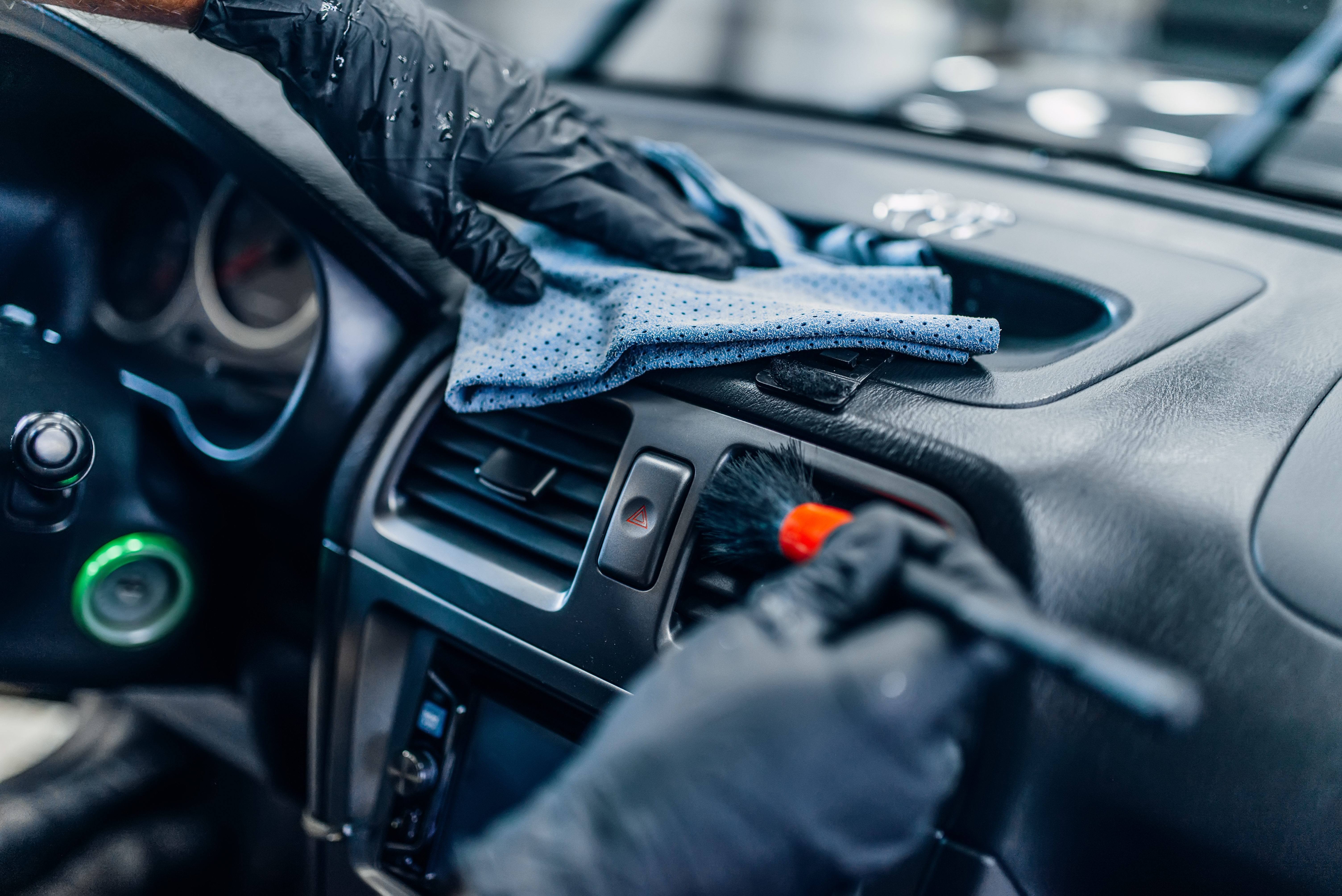 Professional cleaning a car dashboard with microfiber cloth wearing black gloves