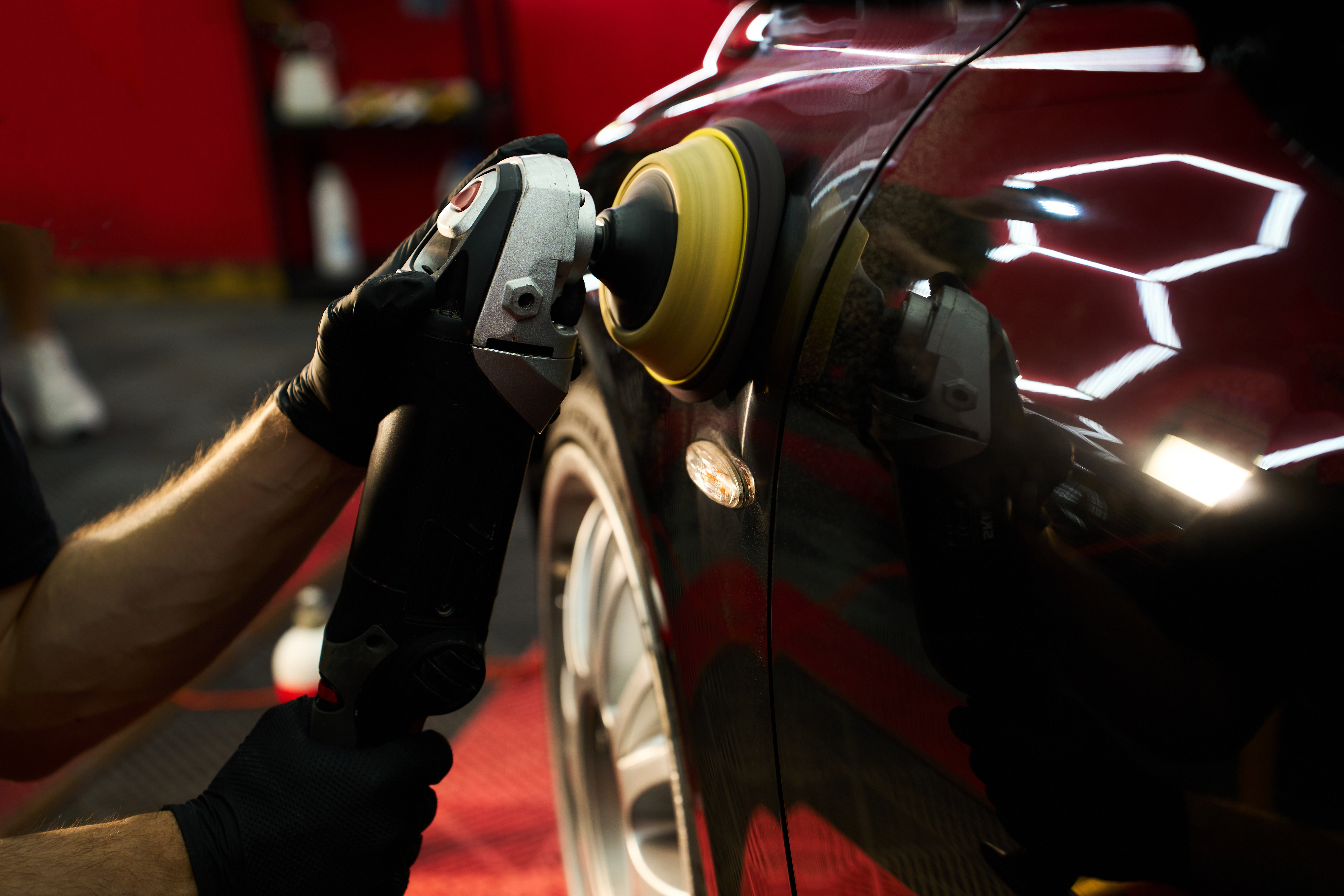Professional using orbital polisher on red car exterior in detail shop