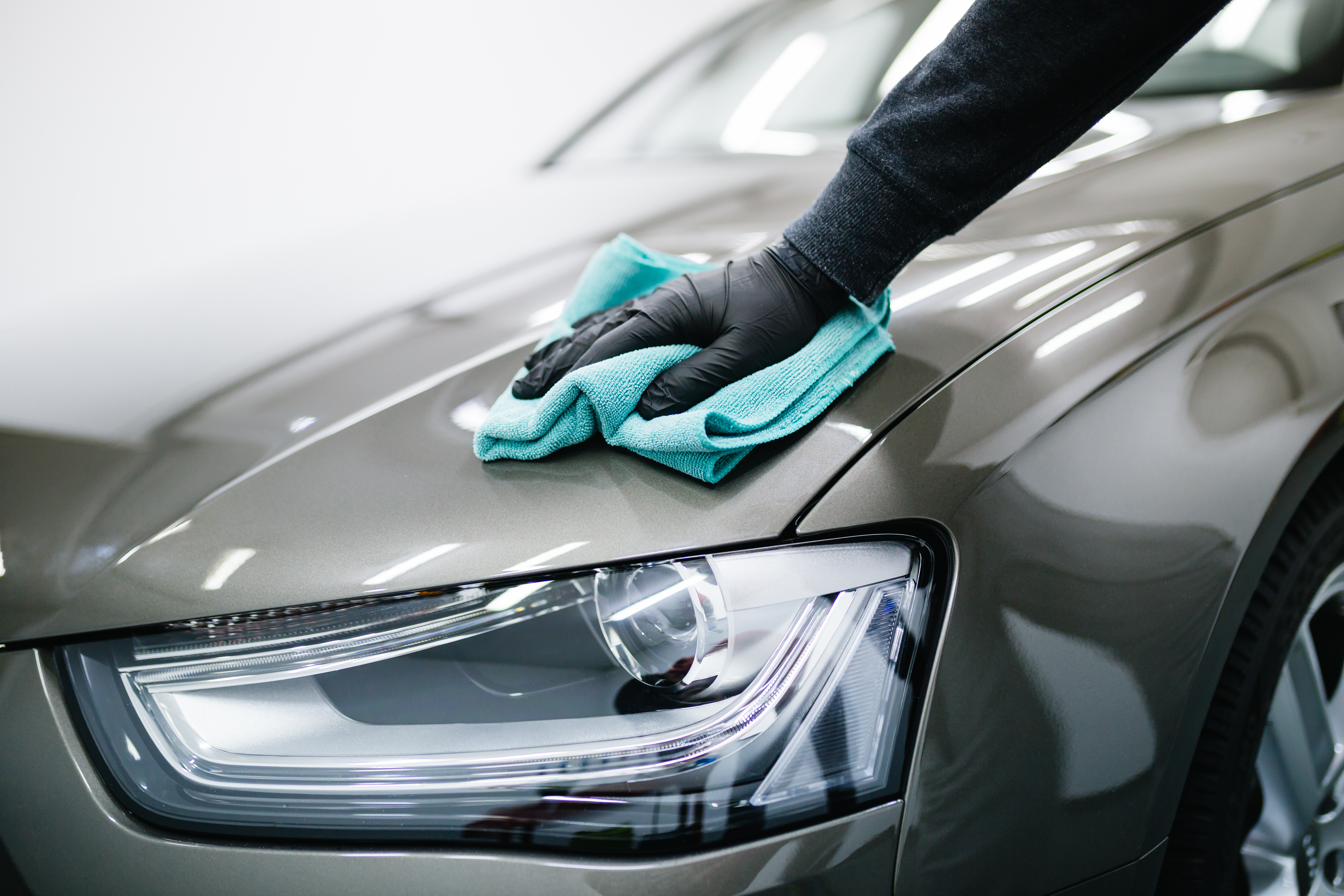Person in black gloves polishing silver car hood with turquoise microfiber cloth