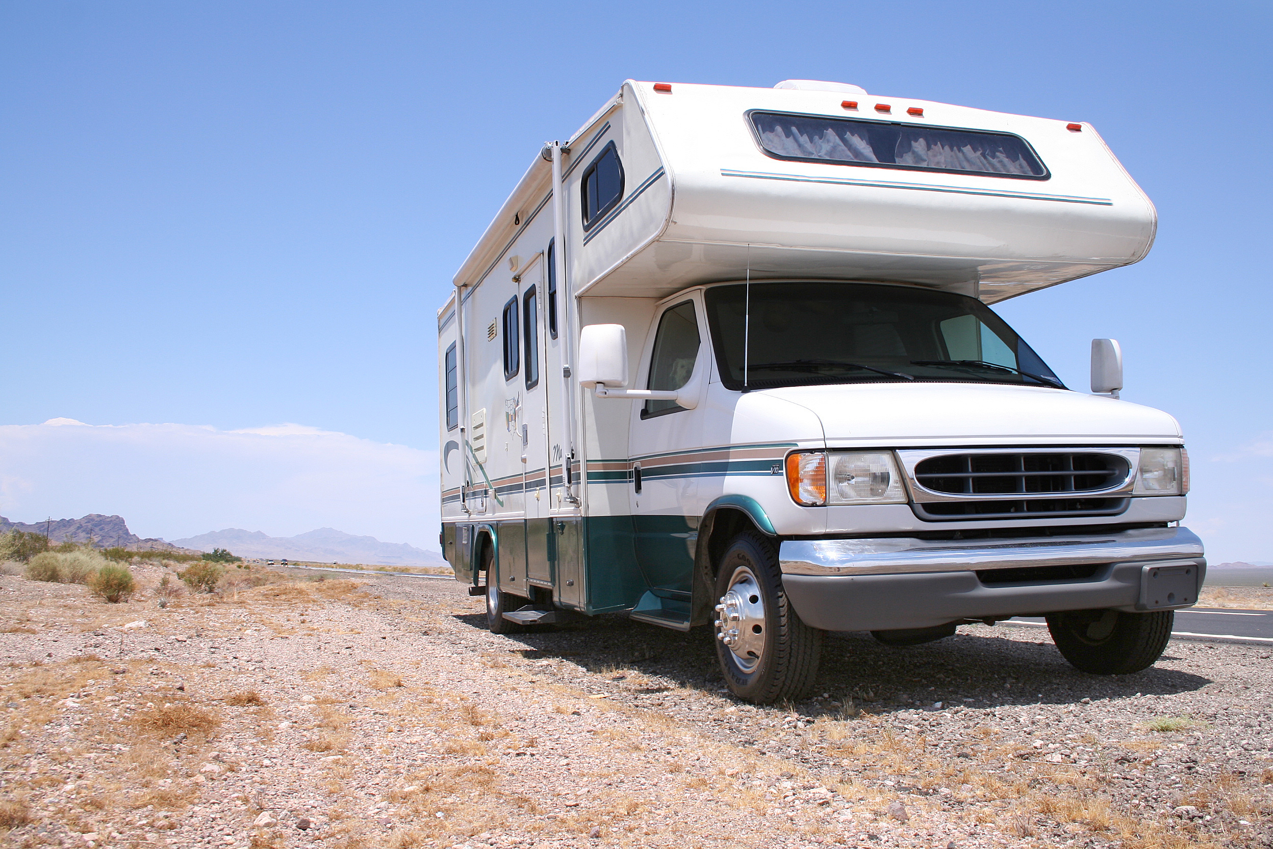 White and green RV camper parked on desert terrain with mountains in background